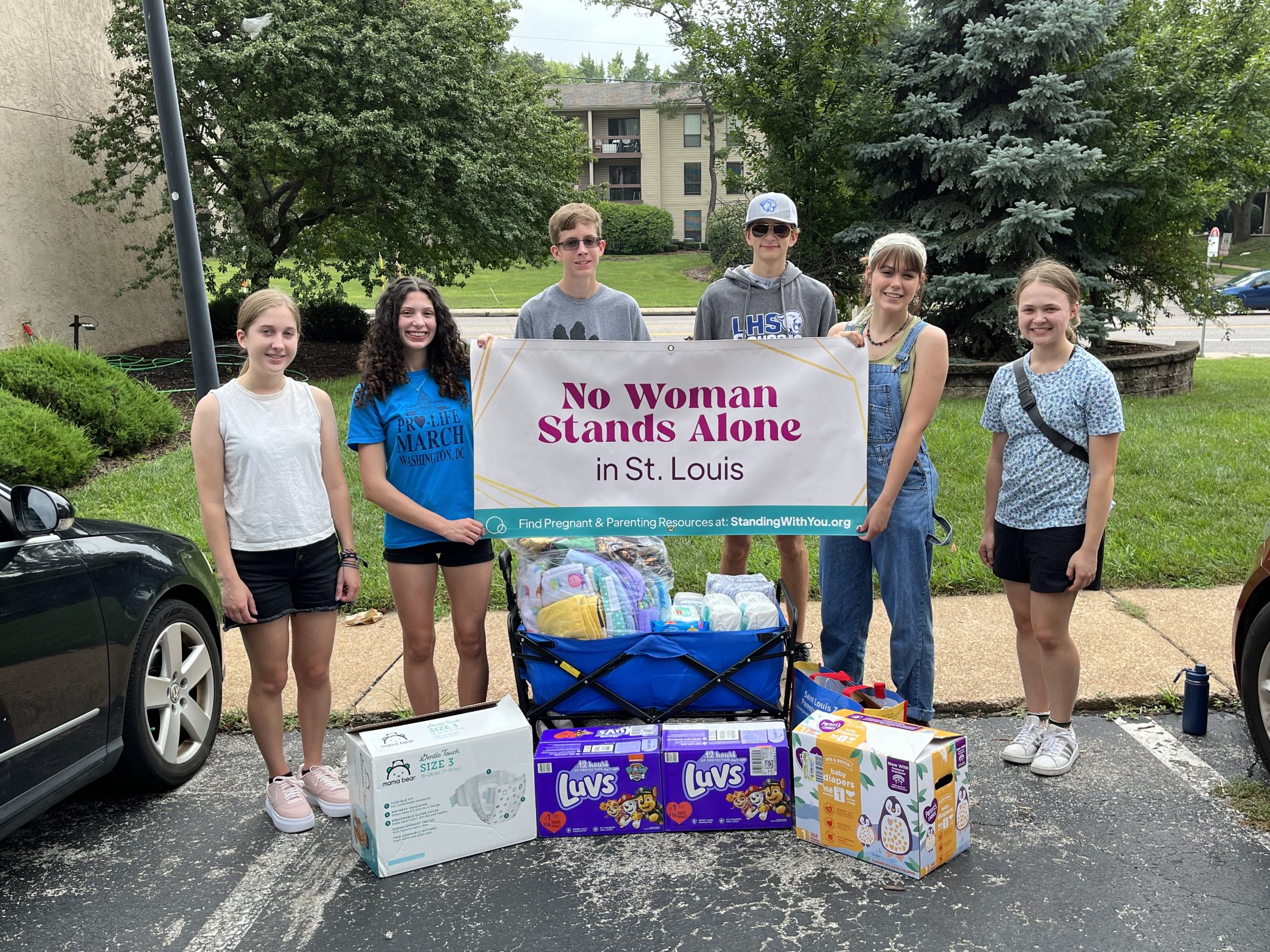 A group of people are standing and holding a sign together while looking at the camera.
